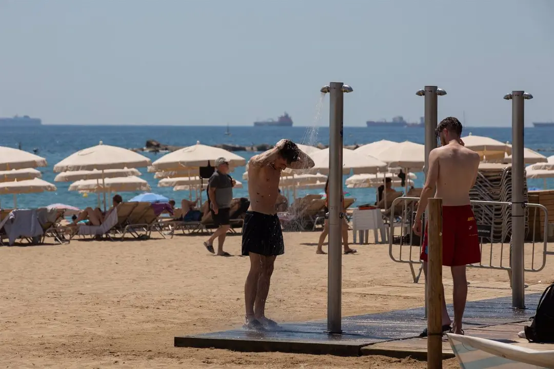 Varias personas se mojan en las duchas de la playa de la Barceloneta / Europa Press