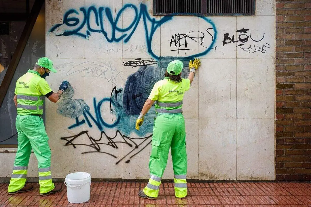 Dos t&eacute;cnicos de limpieza borrando grafitis de una pared ./ Ayuntamiento de Zaragoza
