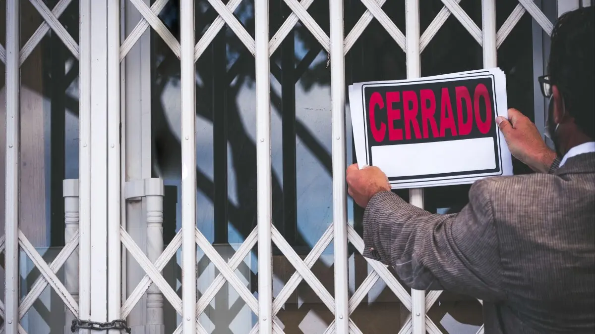 Archivo - Un hombre cuelga el cartel de cerrado e un local
