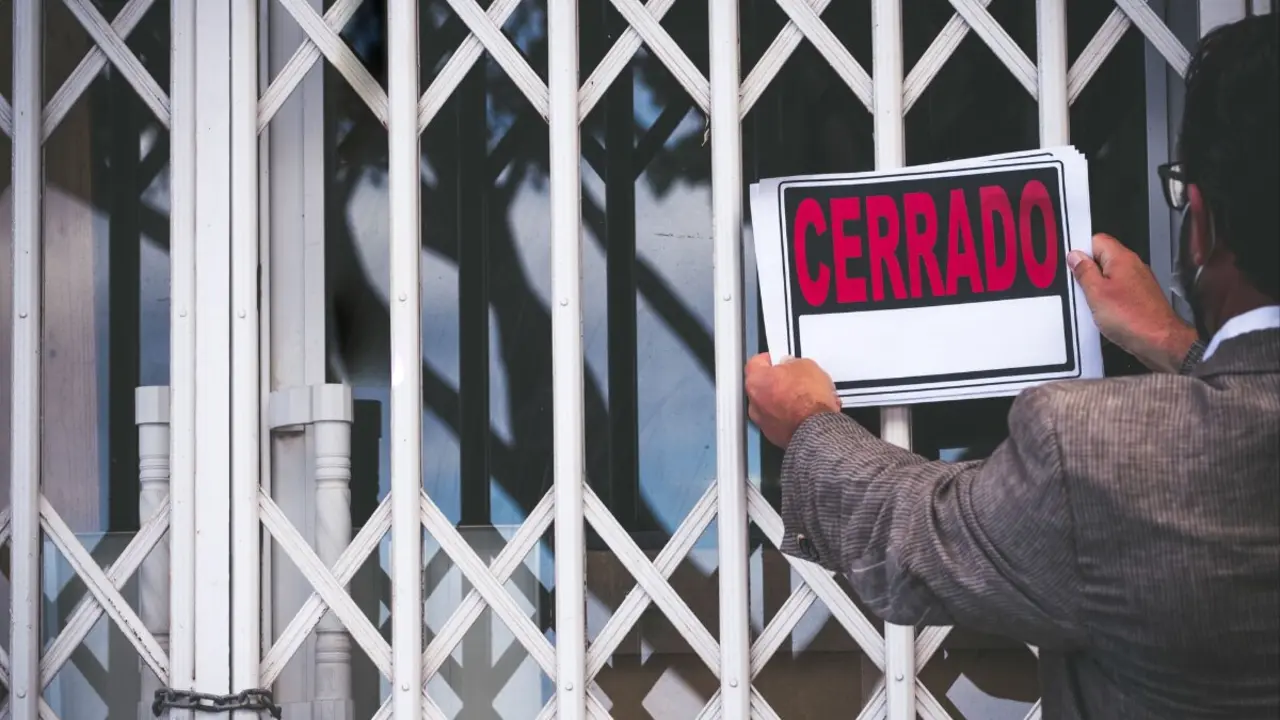 Archivo - Un hombre cuelga el cartel de cerrado e un local