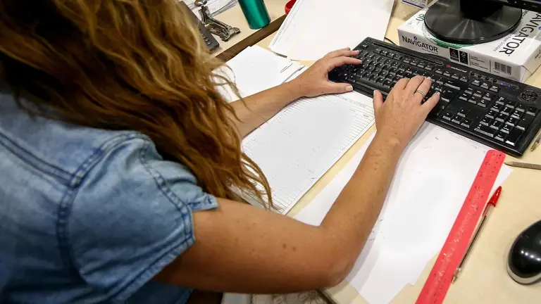 Una mujer escribe en el teclado de su ordenador, con papeles alrededor mientras trabaja en la oficina. / E.P.