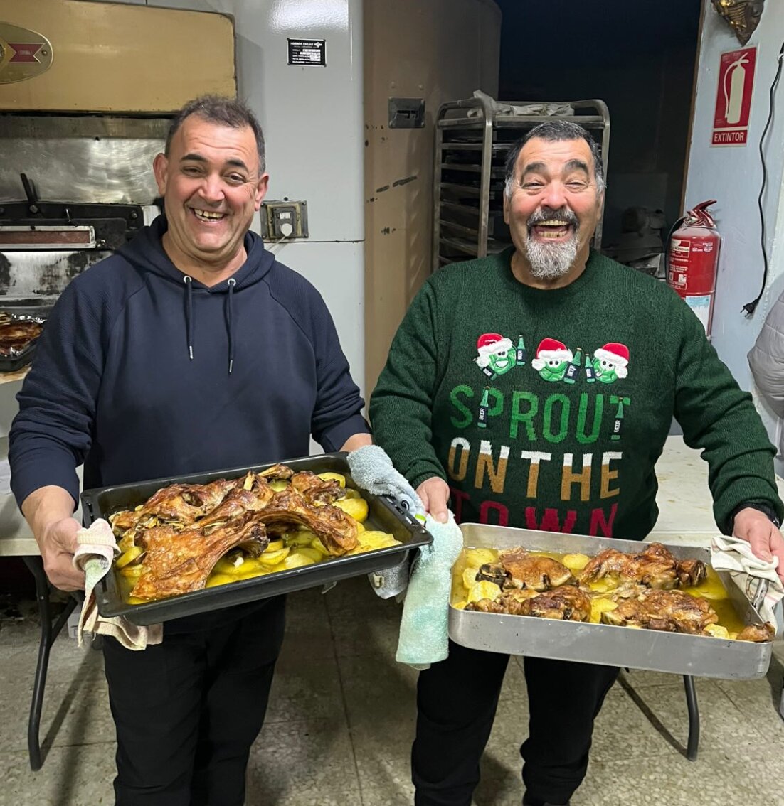 Dos vecinos sonrientes al recoger el asado preparado en el horno de Luis Ángel / Cedida